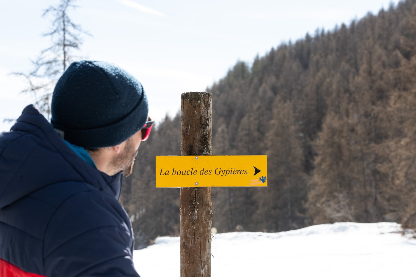 homme devant un panneau de randonnée en hiver